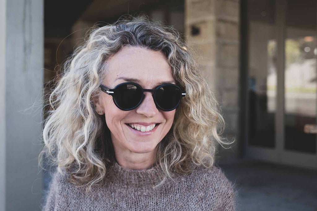 Smiling woman wearing Good Citizens black round sunglasses, made in Sydney from 100 percent recycled frames.