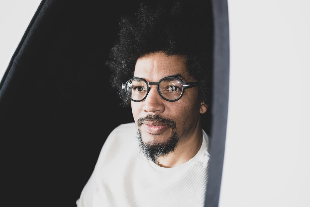 Man wearing Good Citizens round black reading glasses, sitting in a music studio setting, made from 100 percent recycled frames.
